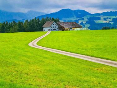 Panoramic view of green hills and Swiss chalets in Appenzell under a clear blue sky.