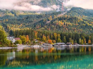 Eibsee, Germany. Autumn foliage around a serene lake with reflections and cable car lines.