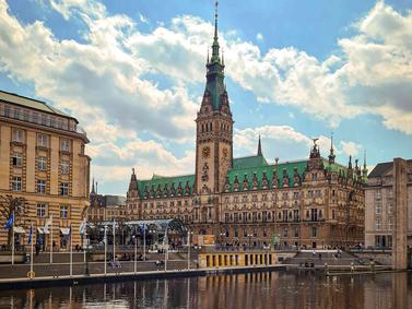 Hamburg, Germany: Hamburg City Hall with Alster River in the foreground under a cloudy sky.