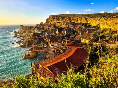 Malta: Coastal village with unique architecture against cliffside at sunset.