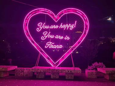Tirana, Albania. Neon-lit heart-shaped installation at night with 'You are happy! You are in Tirana' message.