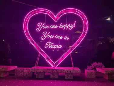 Tirana Travel Guide: Neon-lit 'You are happy!' installation at night, a vibrant city landmark in Albania.